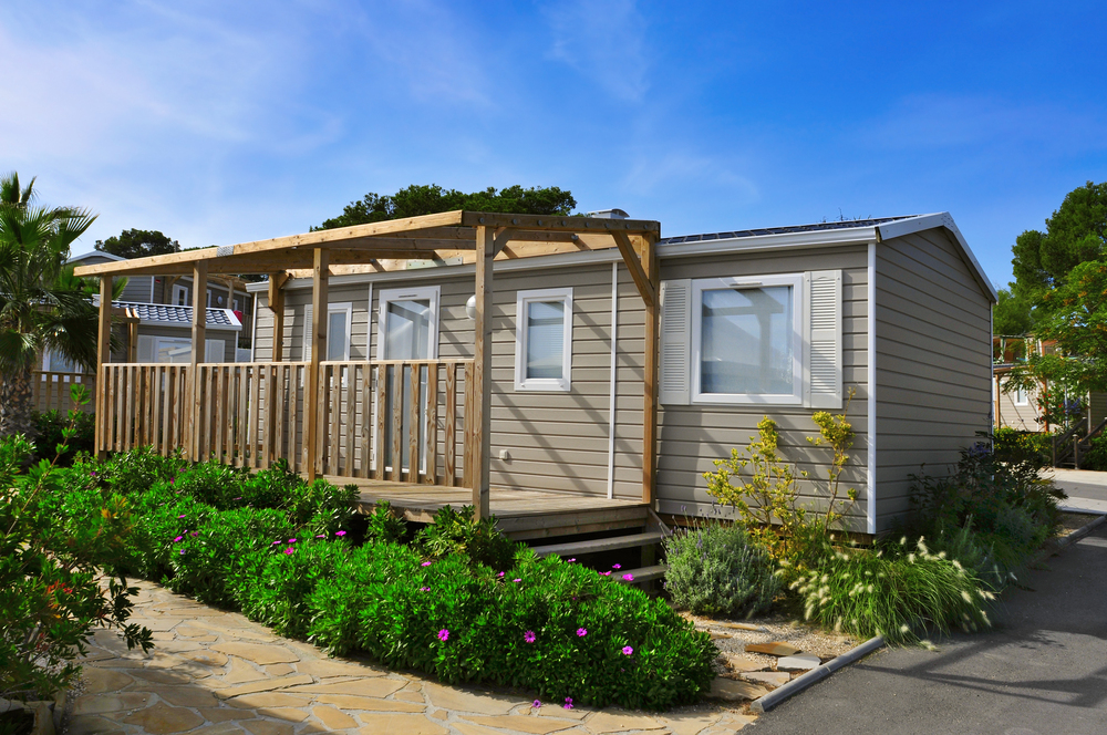 A nice mobile home with a healthy garden and a veranda.